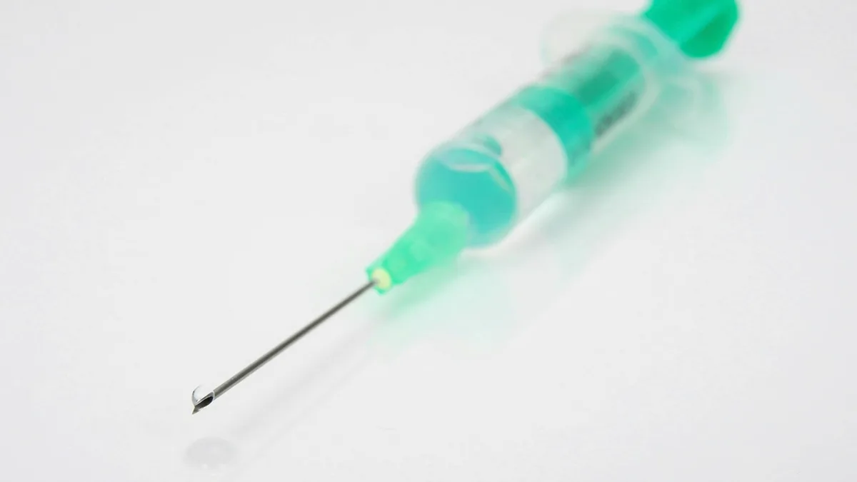 A syringe filled with green vaccine solution resting on a white surface
