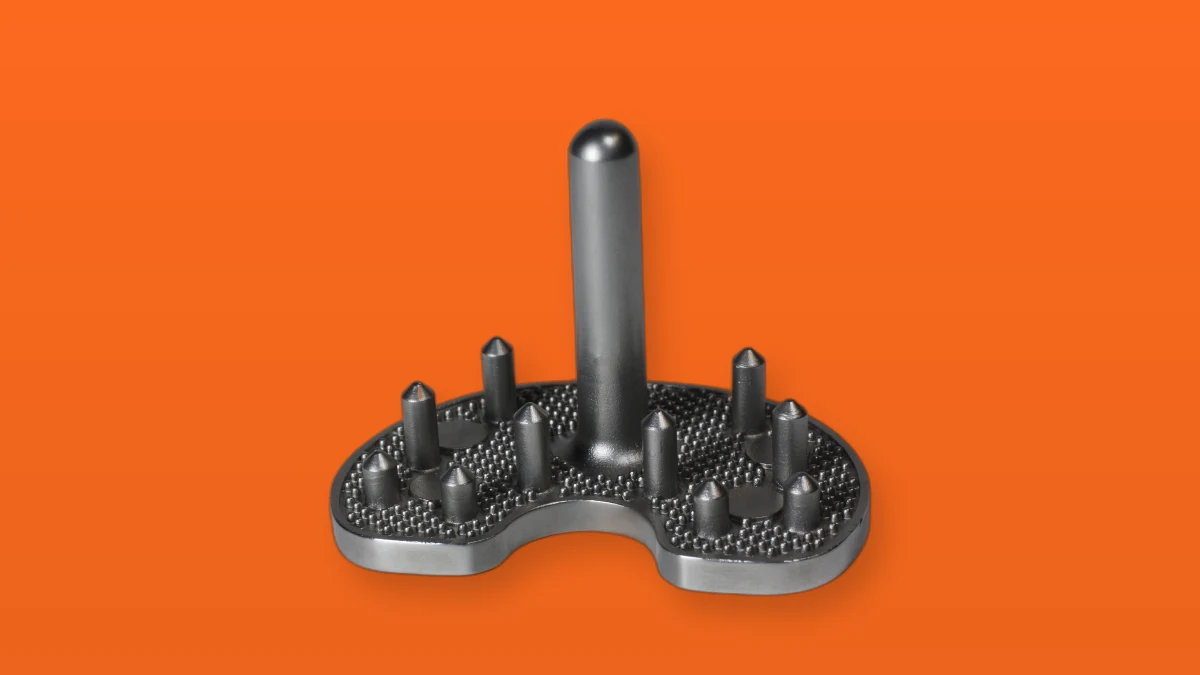 A metal knee joint implant photographed on a bright orange background