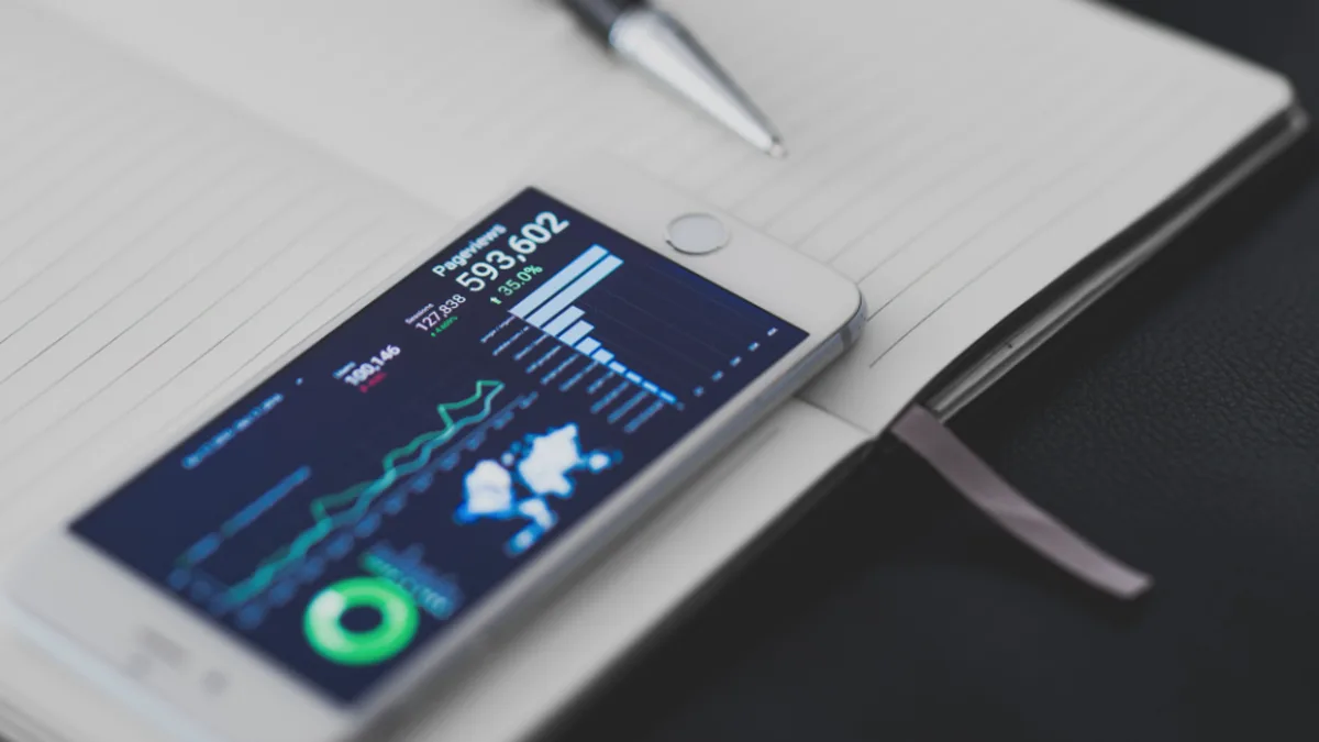 A smartphone displaying a stock trading chart resting on a notebook with a pen