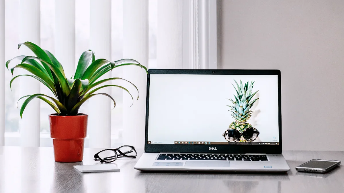 A laptop, potted plant, and eyeglasses on a bright, tidy home-office desk