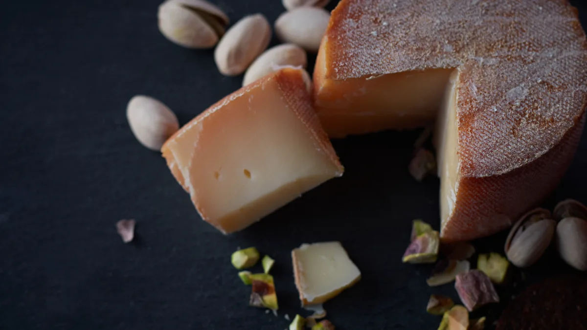 A sharp studio photo of a cut wheel of aged cheese with pistachios on dark slate