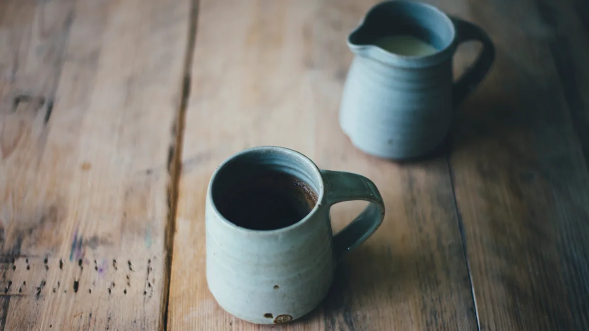 A ceramic coffee mug and a small pitcher on a warm wooden table
