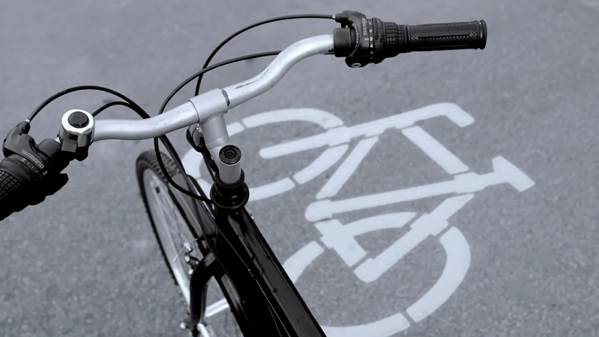 First-person photo of bicycle handlebars over a painted bike-lane symbol on pavement