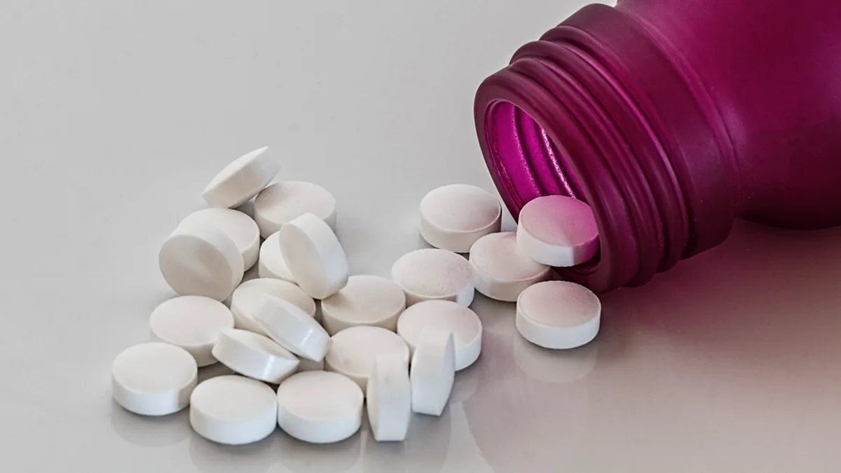 White pills spilling from a magenta prescription bottle
