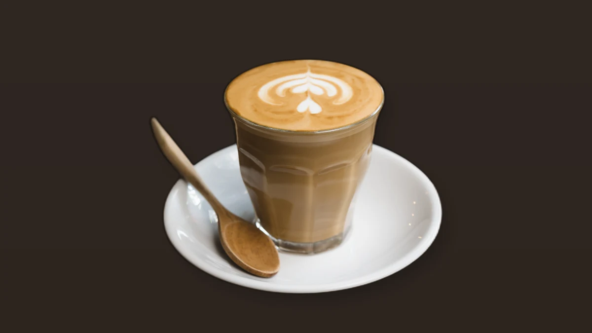 Photo illustration of a latte in a glass on a white saucer with a wooden spoon on a brown background