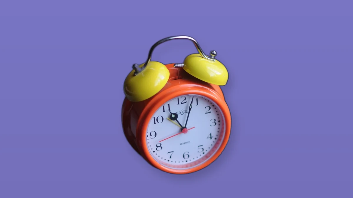 An orange twin-bell alarm clock on a purple background
