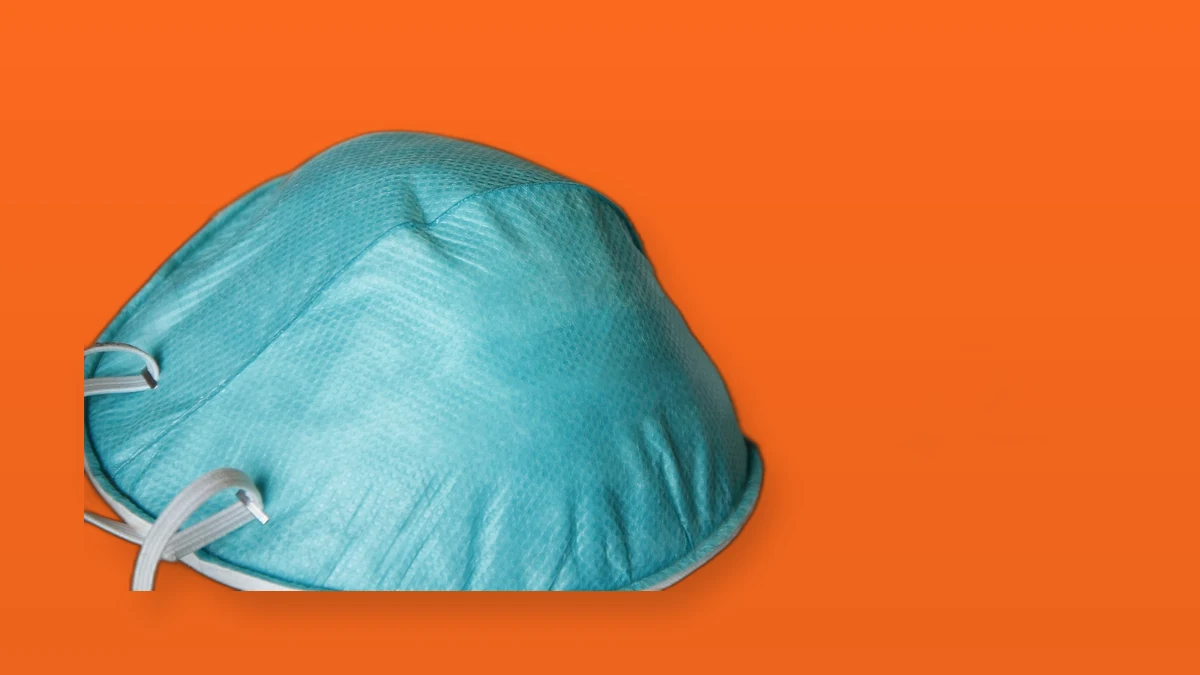 A teal N95 respirator mask on an orange background