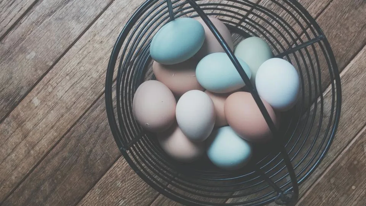 Pastel-colored eggs in a black wire basket on a wooden floor