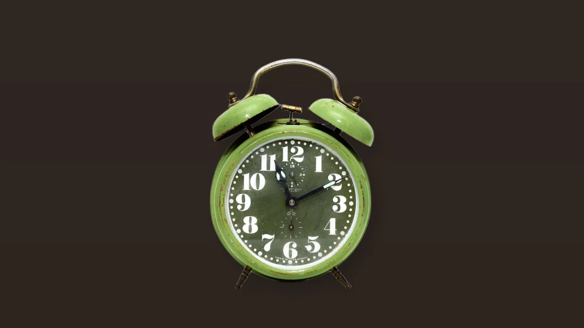 Vintage green twin-bell alarm clock on a dark brown background