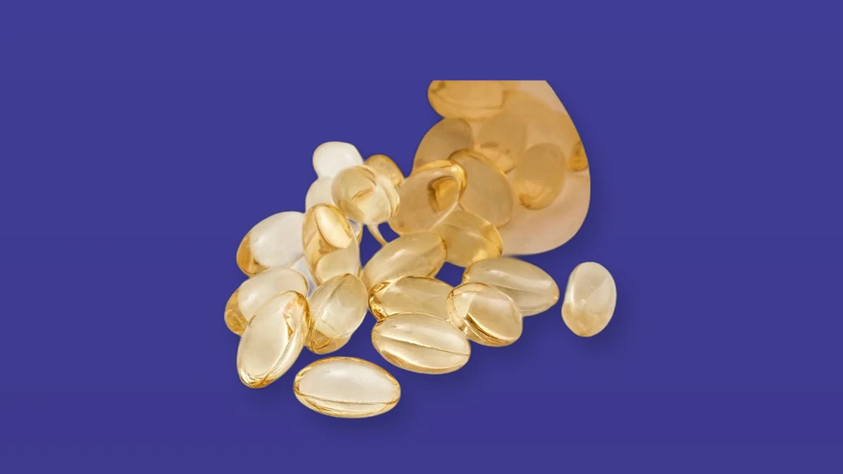 Golden vitamin D softgel capsules spilling from a bottle on a violet background