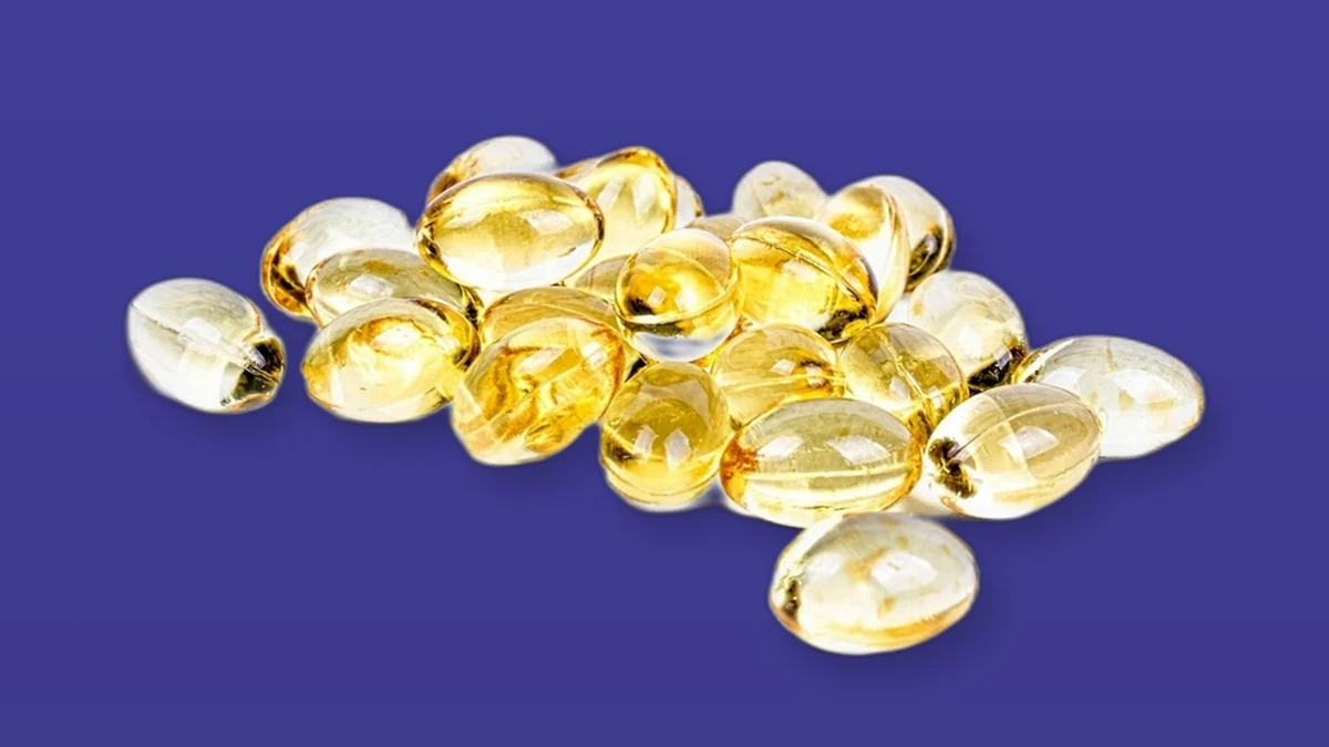 Yellow vitamin D softgel capsules on a violet background