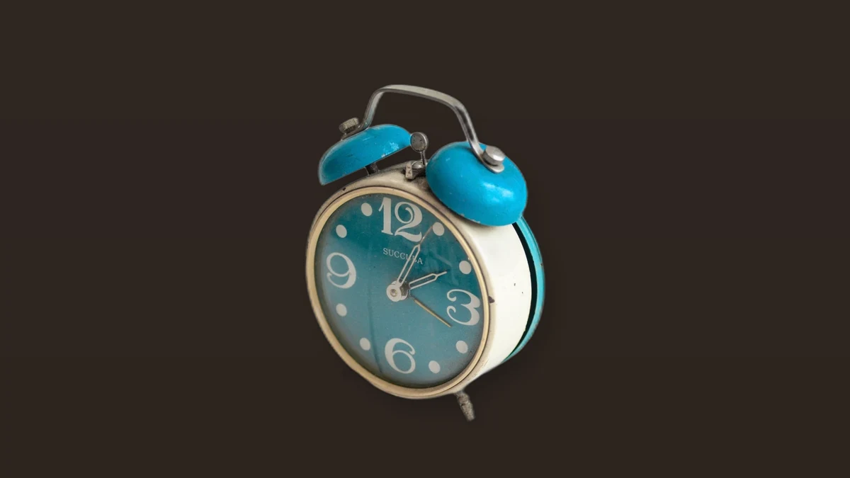 A vintage teal twin-bell alarm clock on a dark brown background