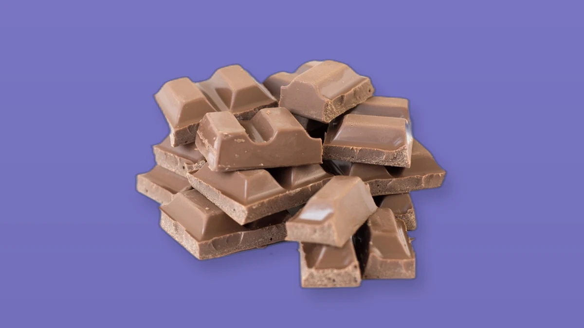 Photo illustration of a pile of milk chocolate pieces on a lavender background