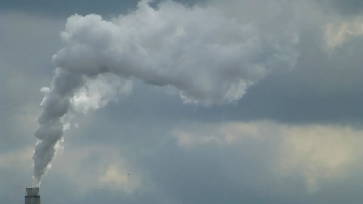 A factory smokestack releasing a large plume beneath a cloudy sky.