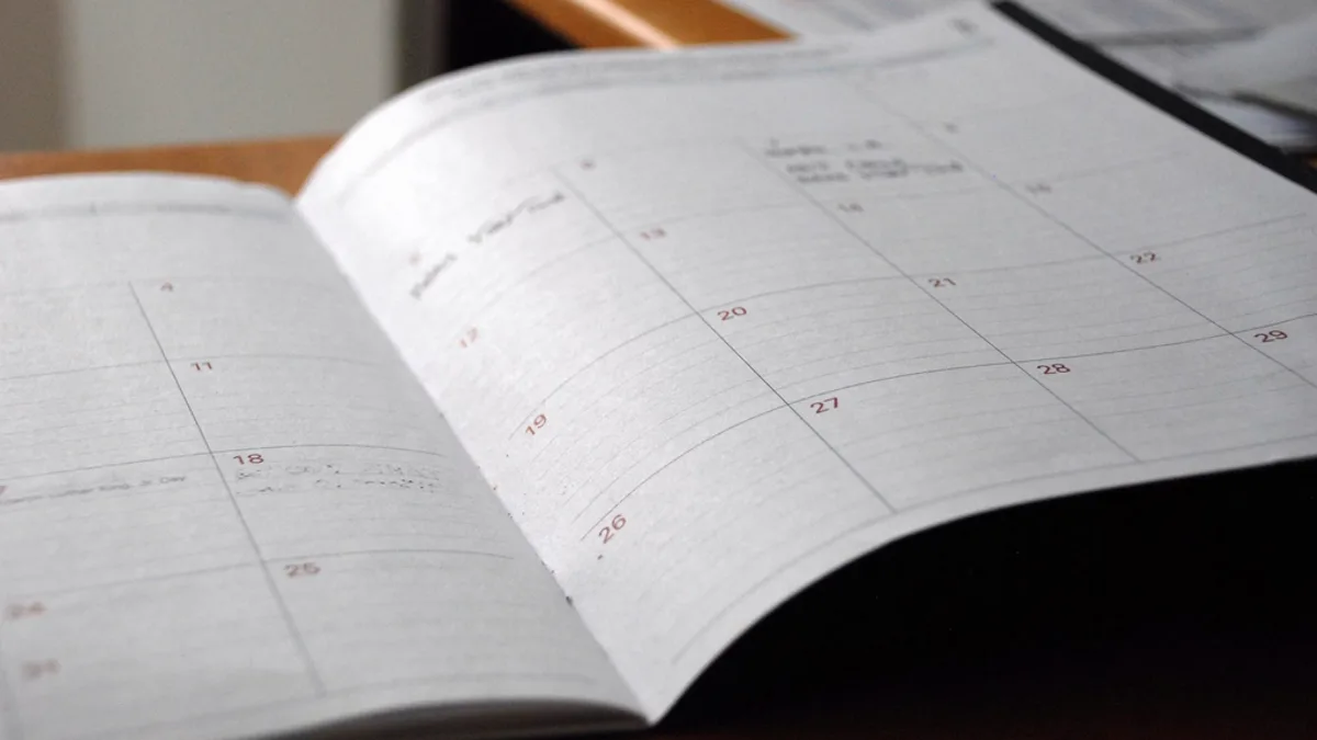 An open paper calendar planner resting on a wooden desk.