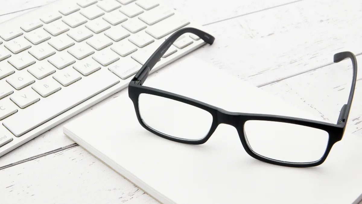 Black reading glasses resting beside a white computer keyboard.