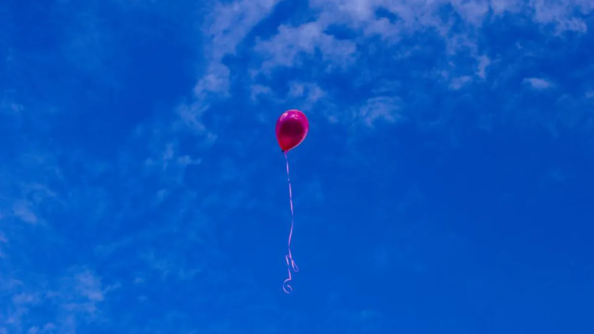 A single red balloon floating against a wide blue sky with wispy clouds