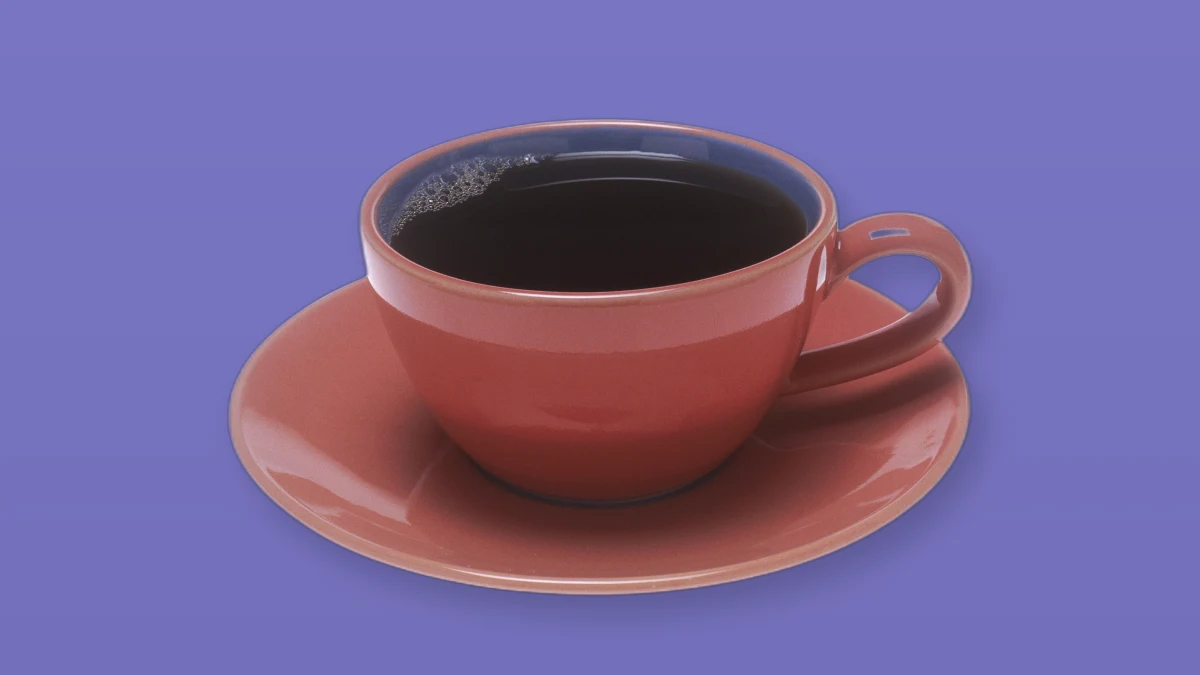 Photo illustration of a red ceramic cup filled with black coffee on a lavender background.