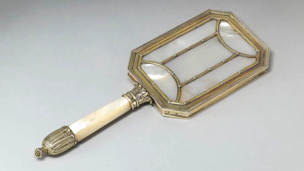 An ornate vintage hand mirror photographed on a pale background
