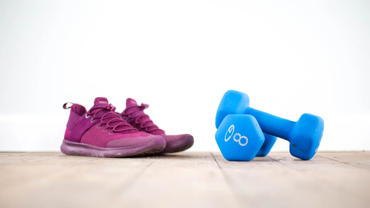 Pink athletic shoes and blue dumbbells arranged on a light wood floor