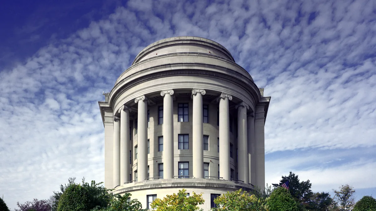 The curved columned facade of the Federal Trade Commission headquarters in Washington, D.C., under a cloud-streaked sky