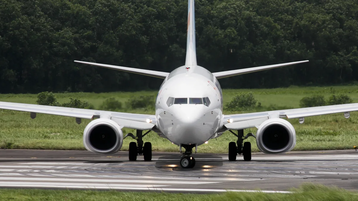 A Flydubai Boeing 737-800 taxiing head-on along a runway lined with trees at Dhaka airport