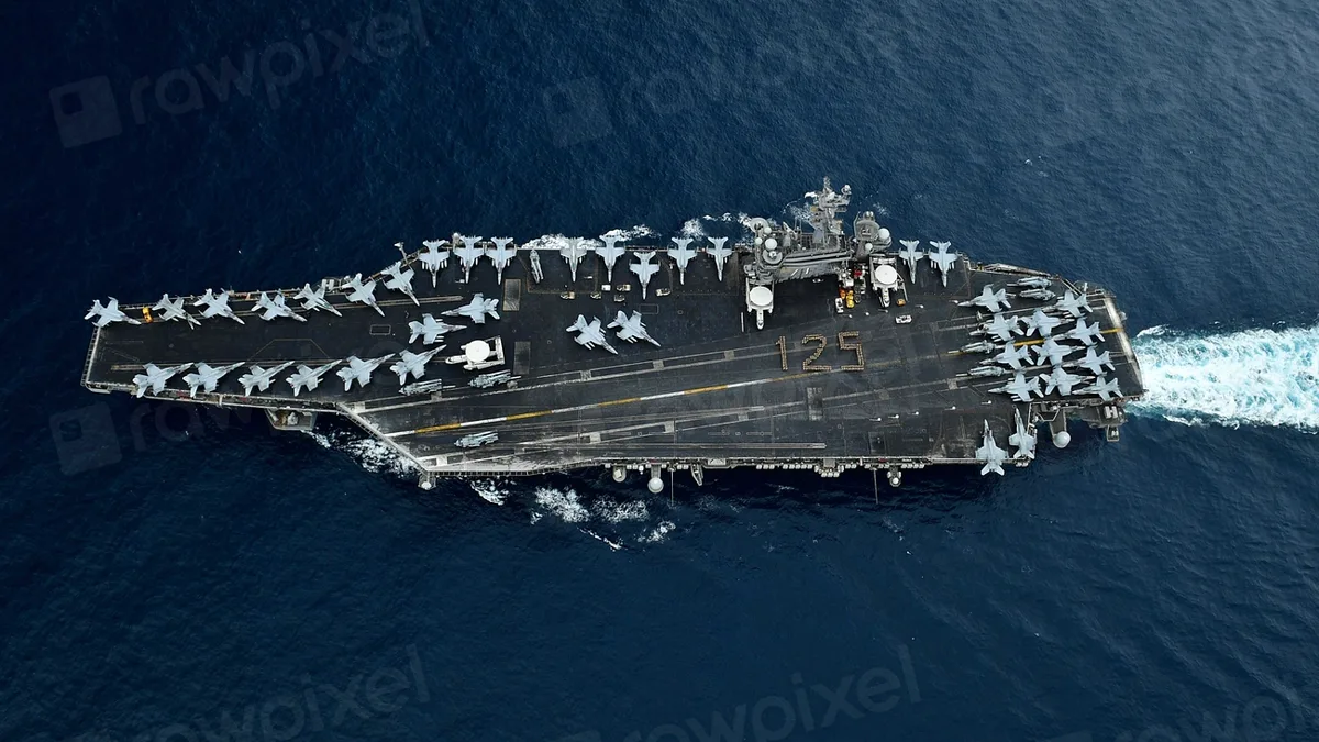 An aircraft carrier under way at sea, seen from directly overhead with jets on deck
