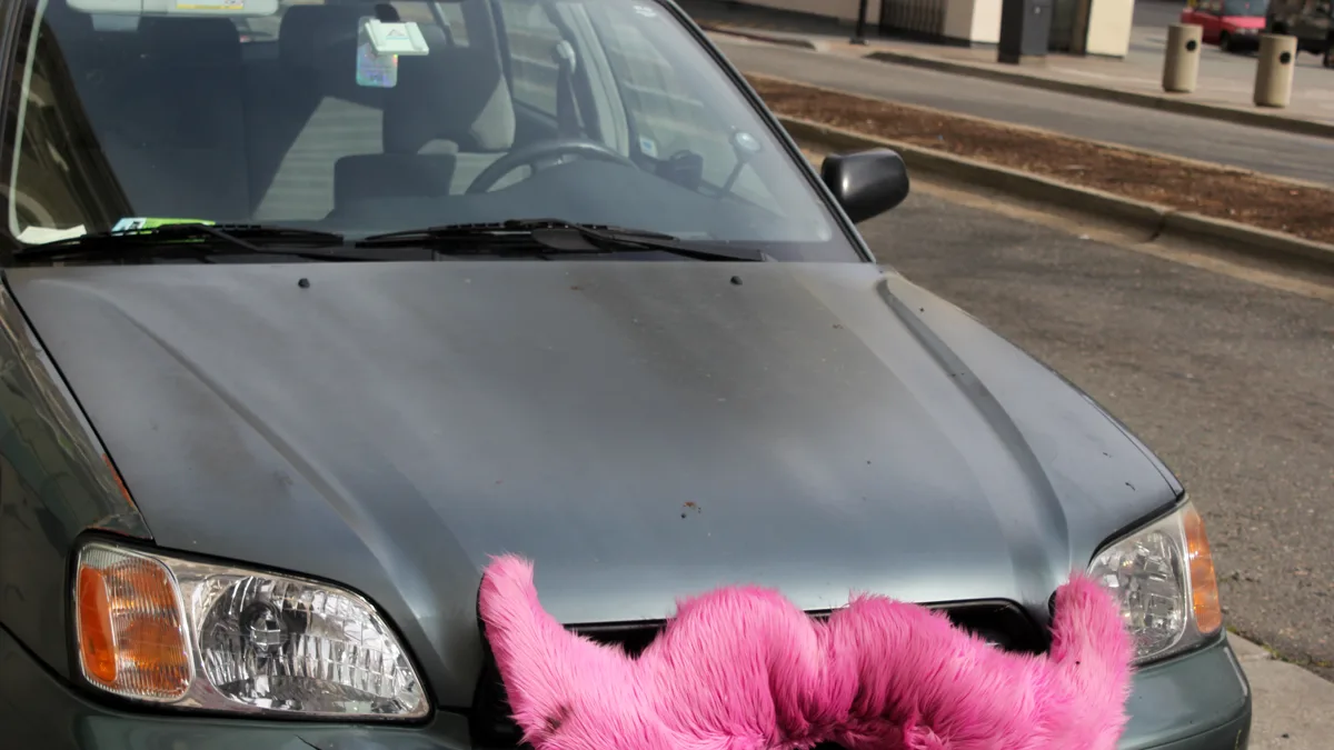 A car parked on a street with the pink furry mustache that Lyft drivers once mounted on the grille