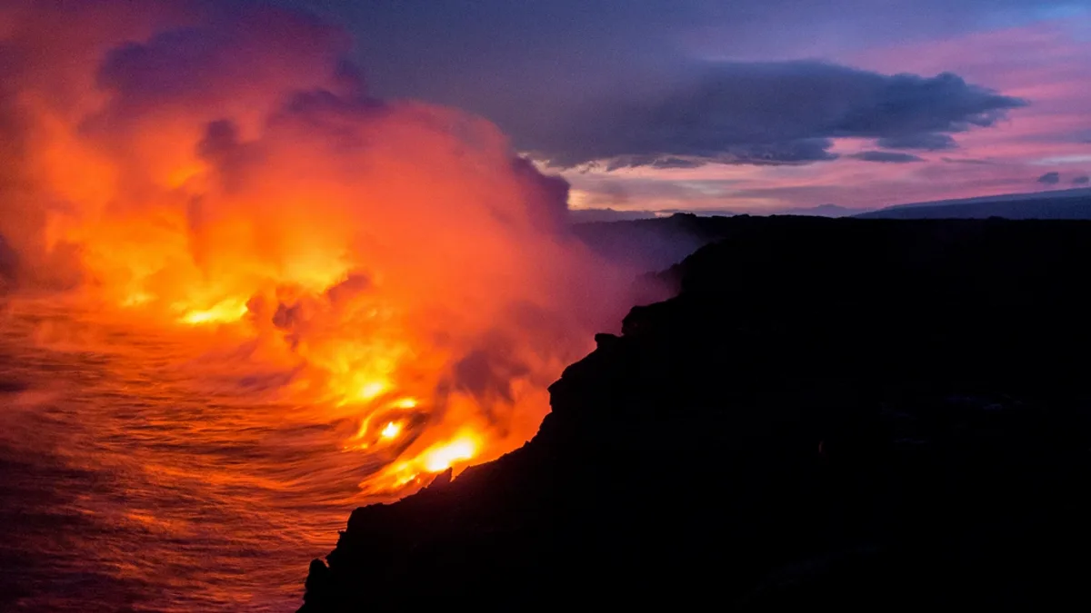 Lava from Kilauea pouring into the Pacific Ocean along a dark sea cliff at dusk