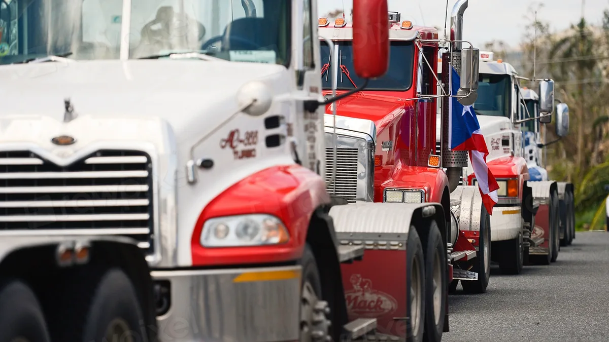 A line of heavy semi trucks parked nose to tail on a roadway