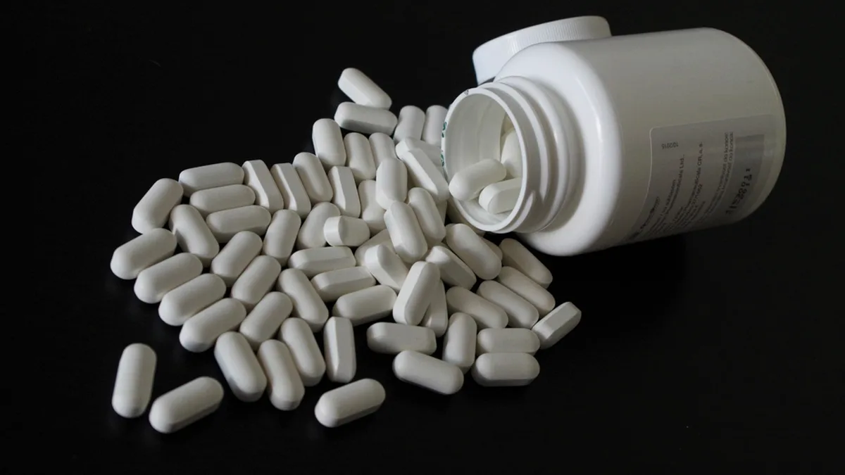 Prescription tablets spilling from a white pill bottle on a dark surface