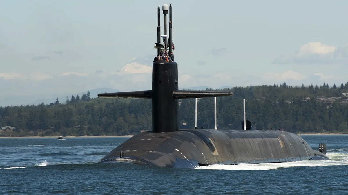 A US Navy nuclear-powered submarine on the surface with a forested shoreline behind it