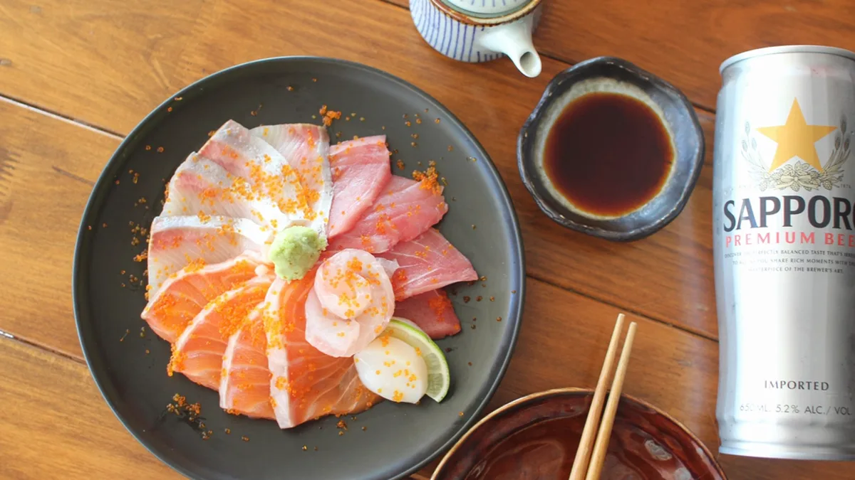 A can of Sapporo premium beer on a wooden table beside a plate of sashimi