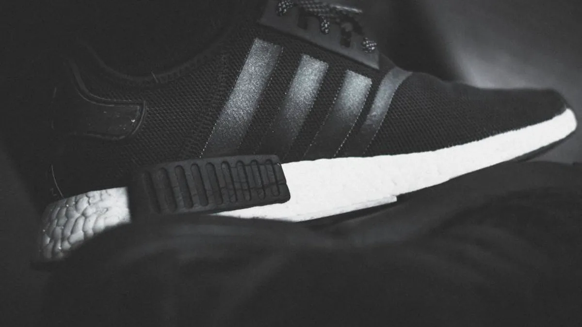 A black Adidas sneaker showing the brand's three parallel stripes along the side