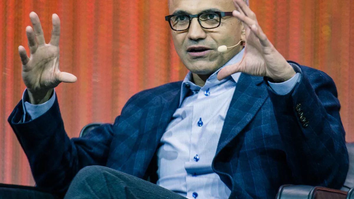 Satya Nadella speaking on stage while wearing a headset microphone