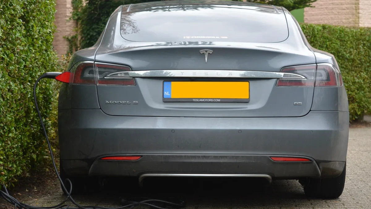 A Tesla sedan plugged in and charging, seen from behind with a European license plate