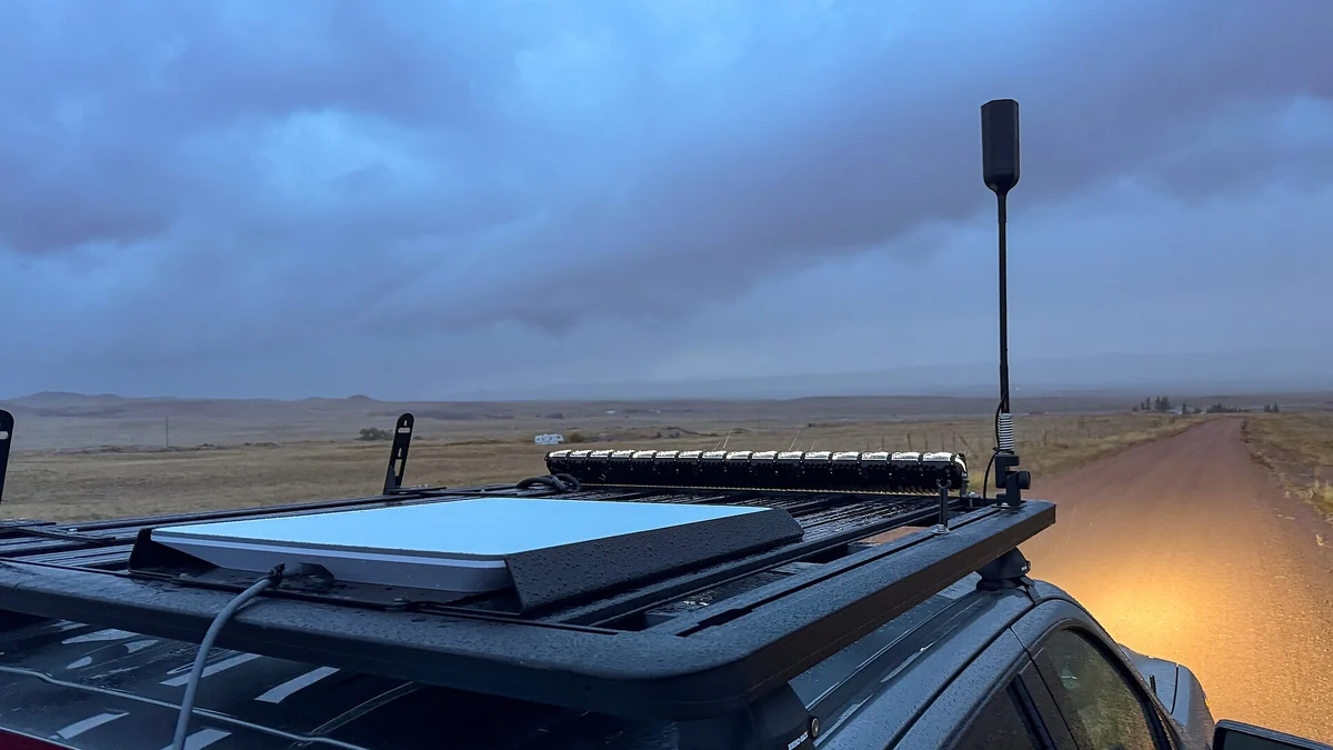 A flat panel Starlink dish mounted on the roof rack of a vehicle on a dirt road
