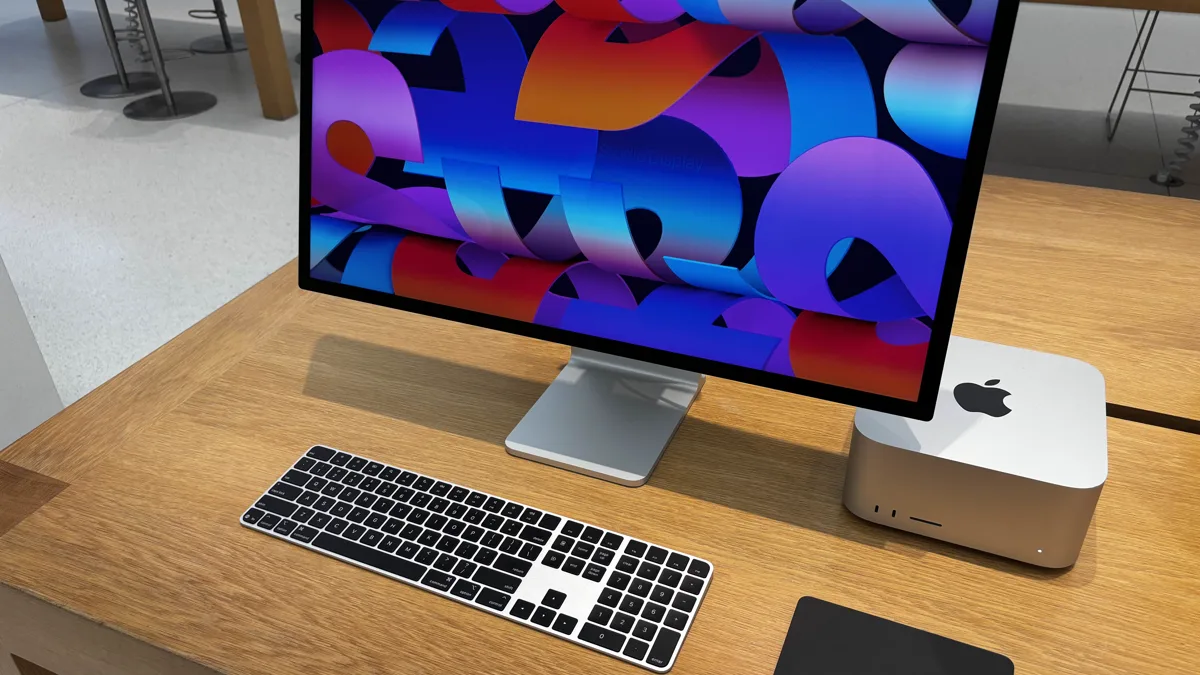 An Apple Mac Studio desktop computer next to a Studio Display and Magic Keyboard on a wooden desk