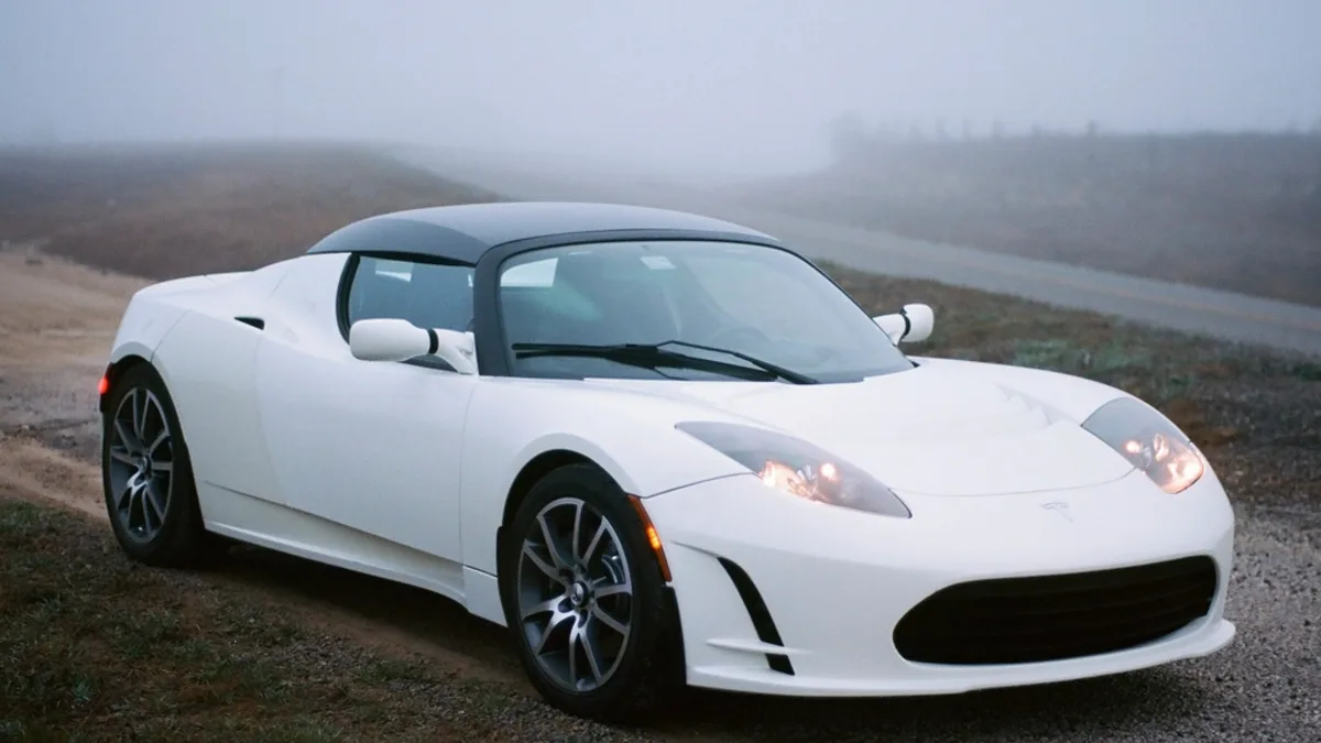 A white first-generation Tesla Roadster parked on a gravel shoulder in morning fog