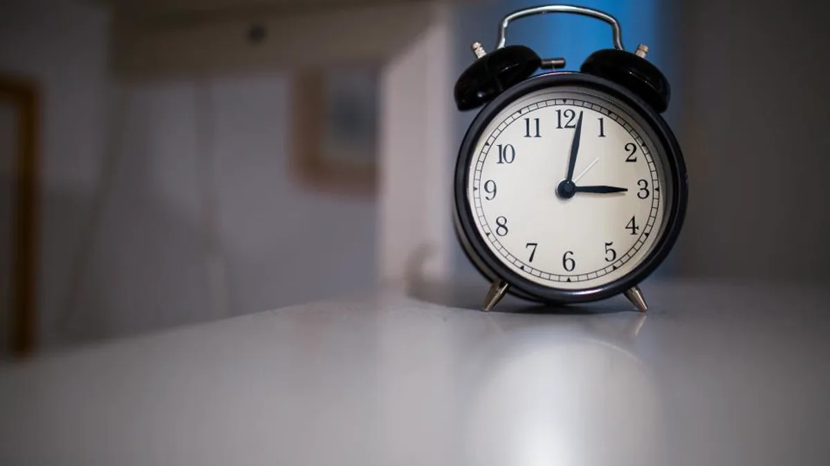 A black analogue alarm clock on a table in dim light