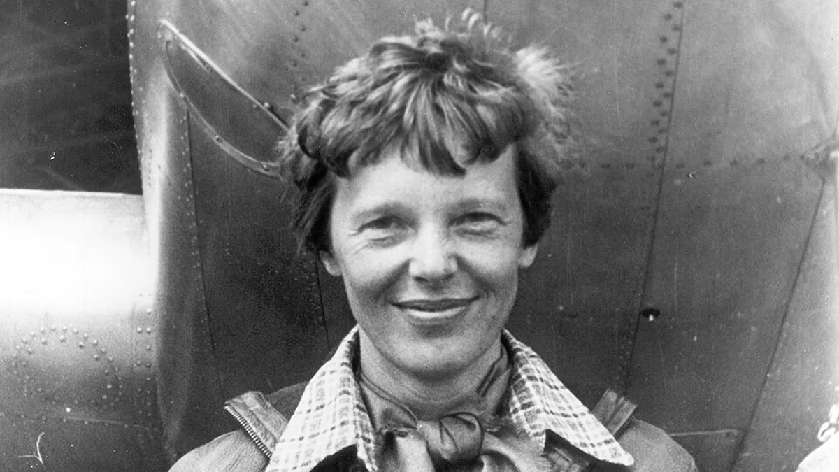 Amelia Earhart smiling in front of the metal fuselage of her aircraft
