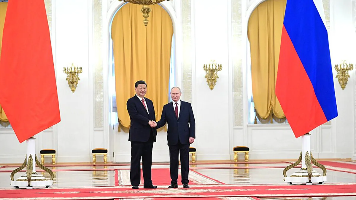 Vladimir Putin and Xi Jinping shake hands between Chinese and Russian flags in a Kremlin hall