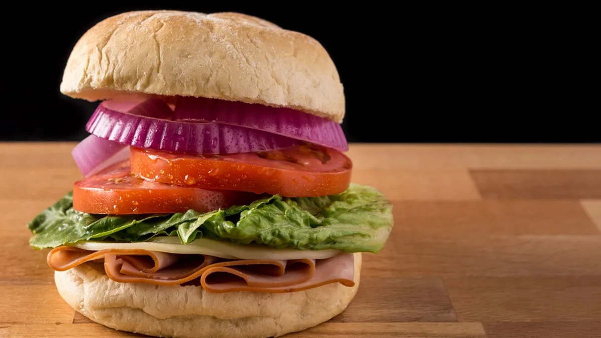 A deli meat sandwich with lettuce, tomato and red onion