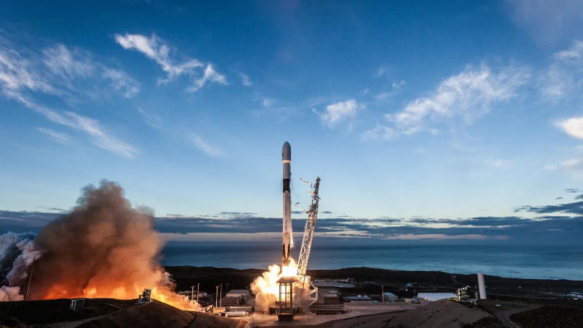 A rocket lifting off from a coastal launch pad at dusk