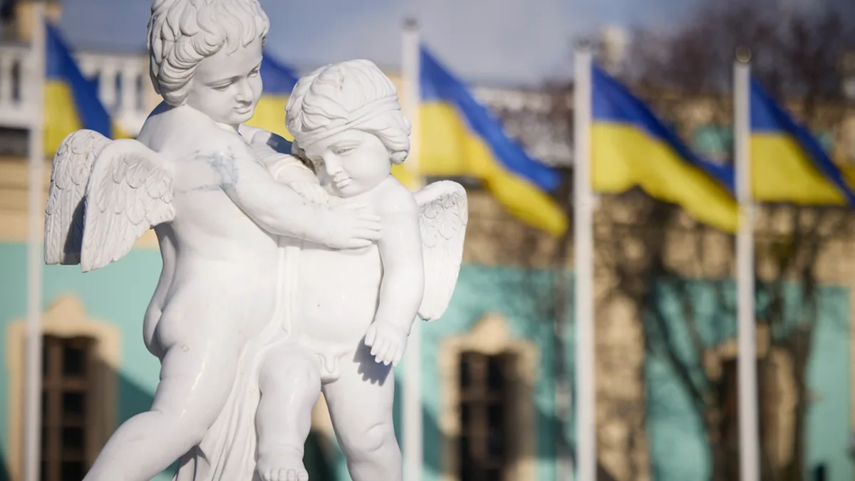 Ukrainian flags behind a white statue of two cherubs