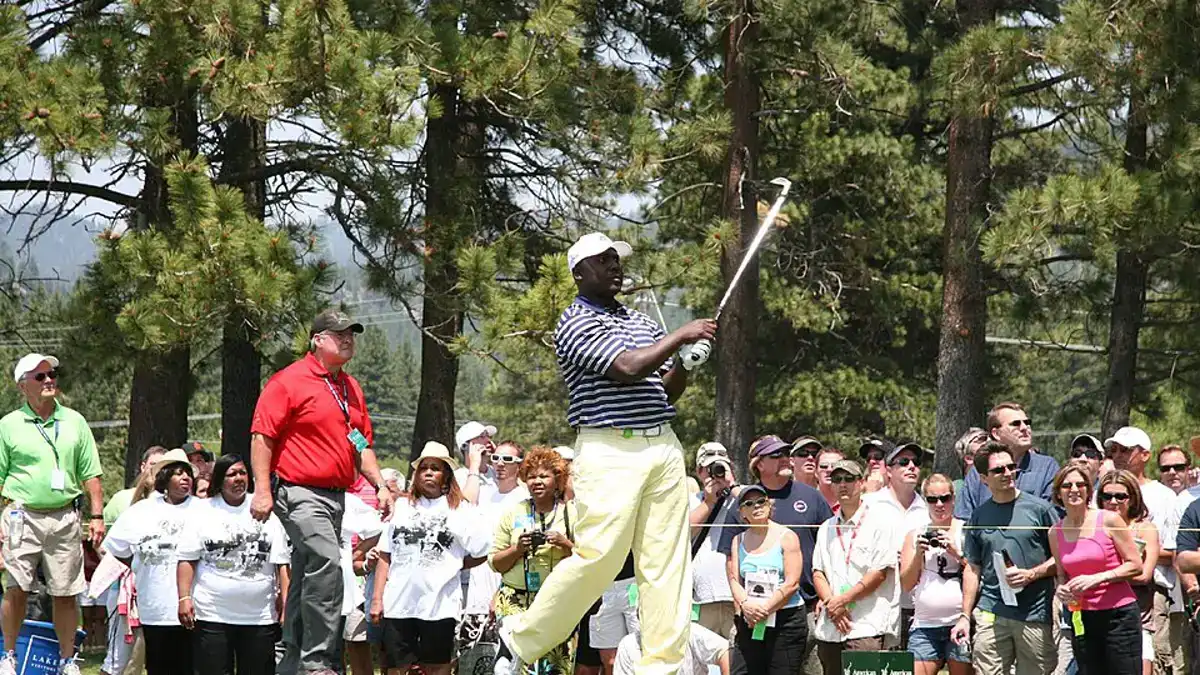 Marshall Faulk following through on a golf swing at a celebrity tournament with spectators behind him