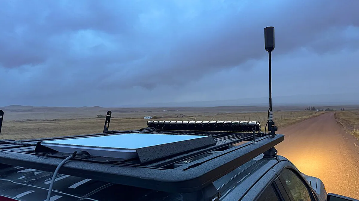 A Starlink flat panel dish mounted on the roof rack of a truck on a dirt road at dusk